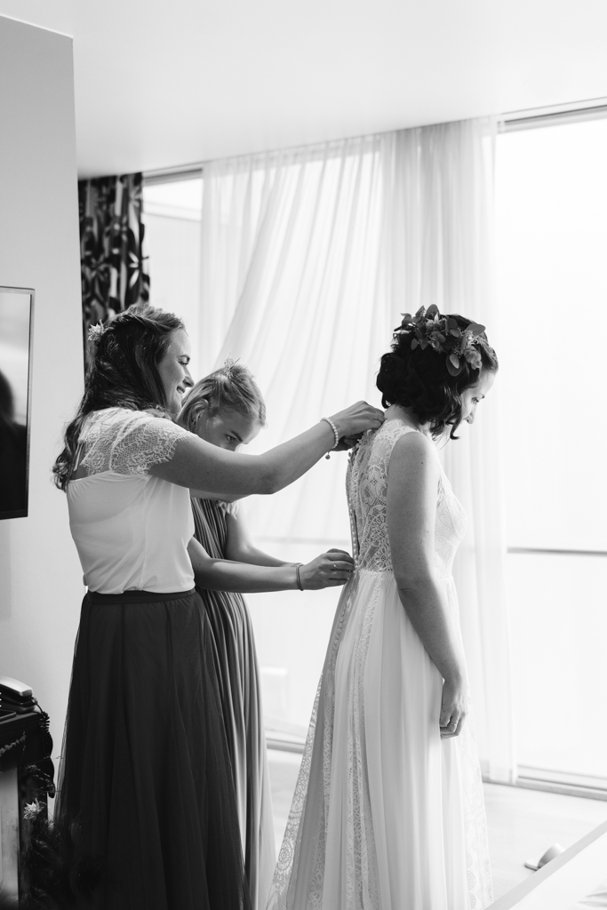 Trauzeuginnen machen das Hochzeitkleid der Braut zu.