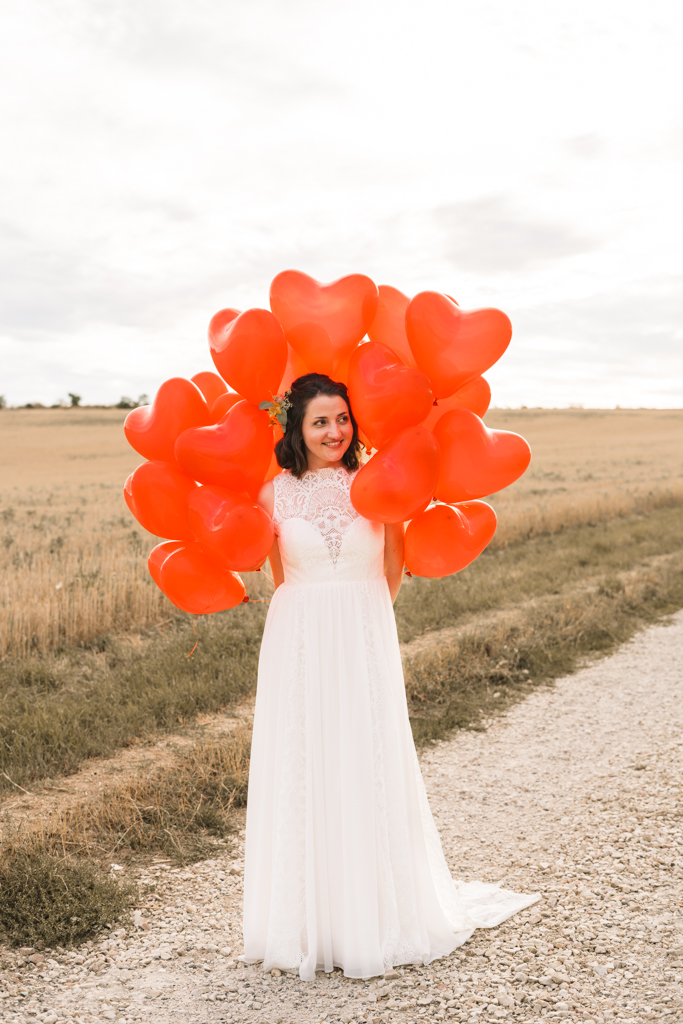 Braut hält rote Herz Luftballons hinter dem Rücken.