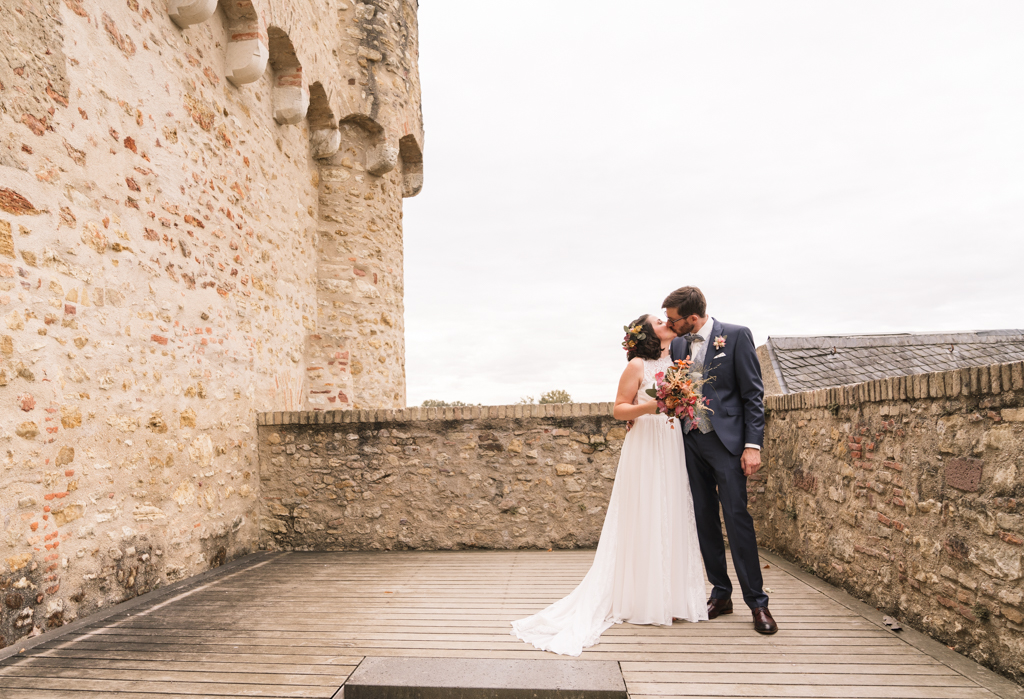 Brautpaar küsst sich auf der Schlossmauer.