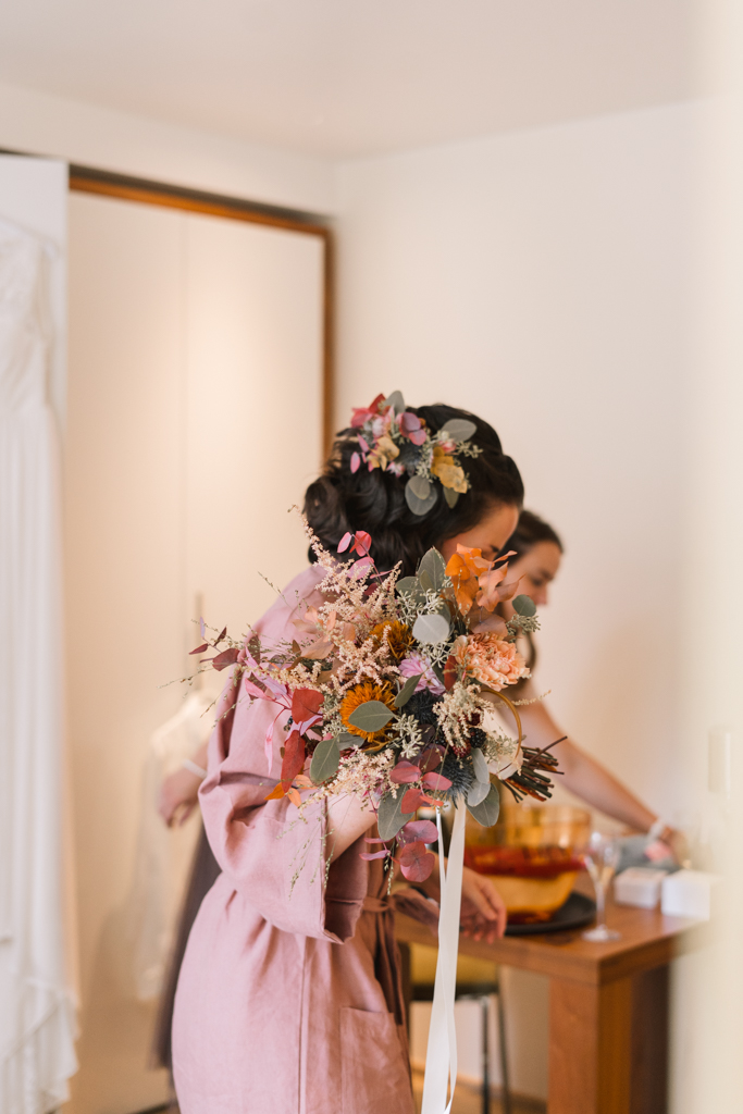 Braut beim Getting Ready mit Hochzeitsstrauß und Blumenhaarschmuck.