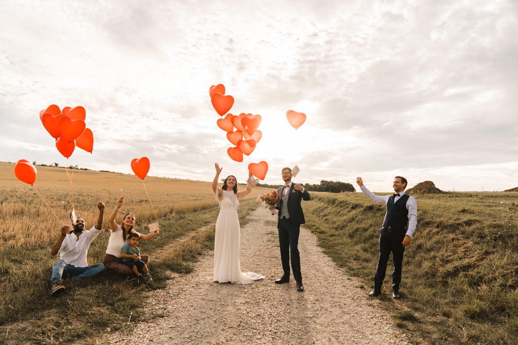 Hochzeitsgesellschaft und das Hochzeitspaar lassen rote Luftballons los.